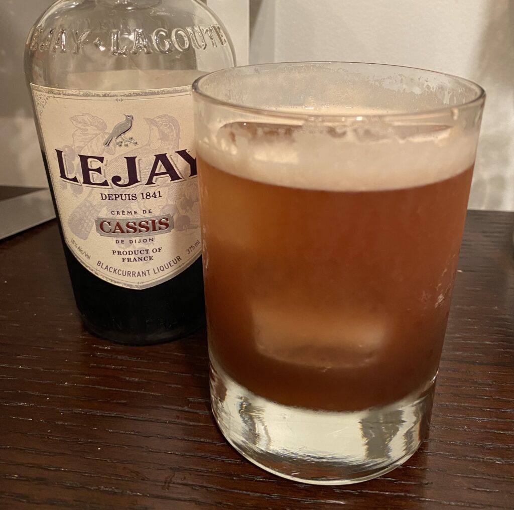 Bourbon Renewal cocktail in an old fashioned glass with a bottle of Lejay creme de cassis